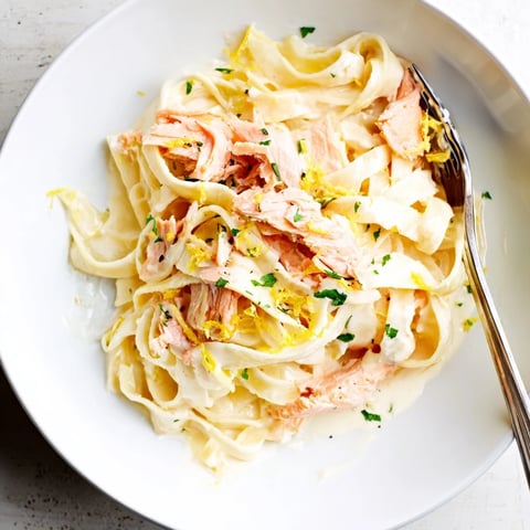 Creamy Salmon Pasta in a skillet, finished with fresh dill and lemon zest beside a glass of white wine.