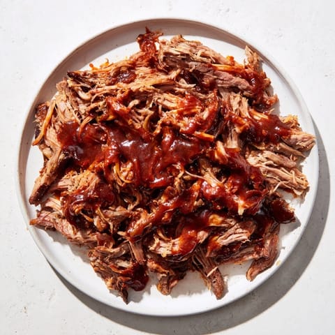 A close-up of slow-cooked 5-Ingredient BBQ Pulled Pork, glistening with barbecue sauce and steam.