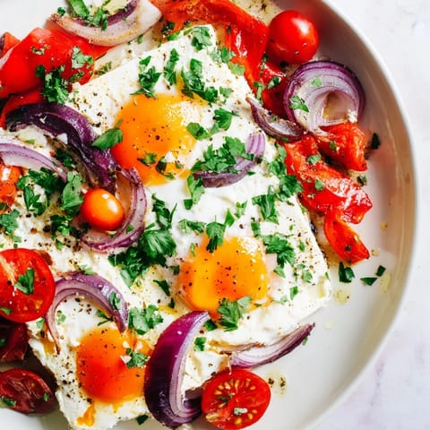 This Mediterranean Baked Feta & Eggs recipe shows golden-yolked eggs amid roasted tomatoes and feta.