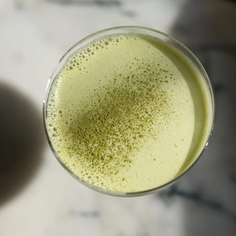 The vibrant green Matcha Martini Cocktail rests beside white chocolate shavings, with a silver shaker and jigger nearby.