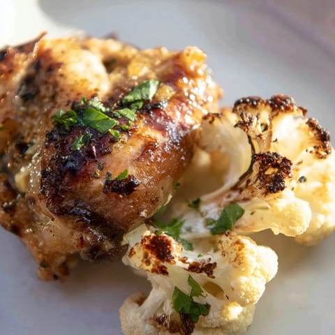 A close-up of the Roasted Cauliflower Chicken Sheet Pan showing tender vegetables and juicy chicken thighs, lightly seasoned with paprika and cumin, ready to be enjoyed over rice.