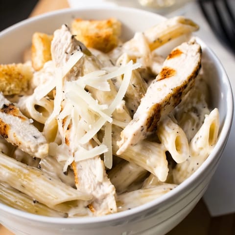A close view shows creamy Caesar dressing coating penne pasta, cherry tomatoes, and grated Parmesan.