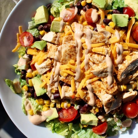 Sliced taco chicken rests on romaine with black beans and cheddar, drizzled with creamy lime dressing for a Tex-Mex meal.