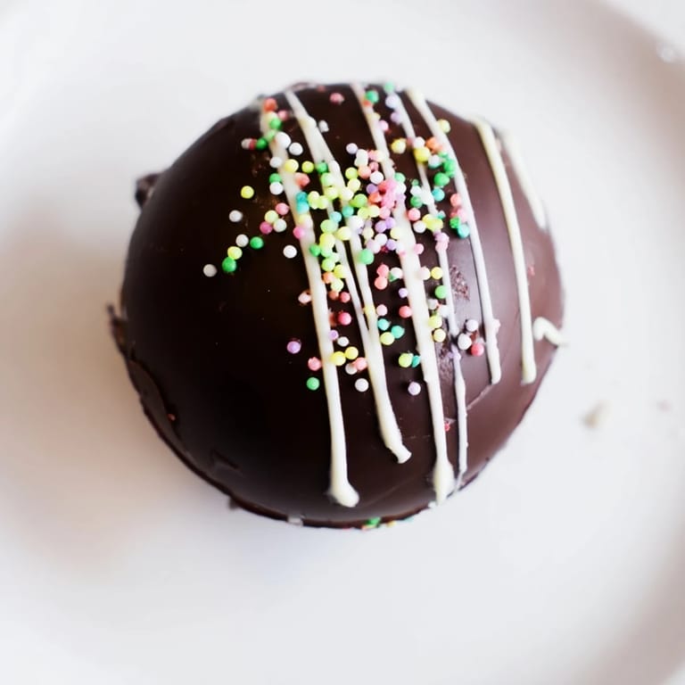 Festive hot chocolate bombs with white chocolate drizzle and colorful sprinkles, perfect for winter gatherings.