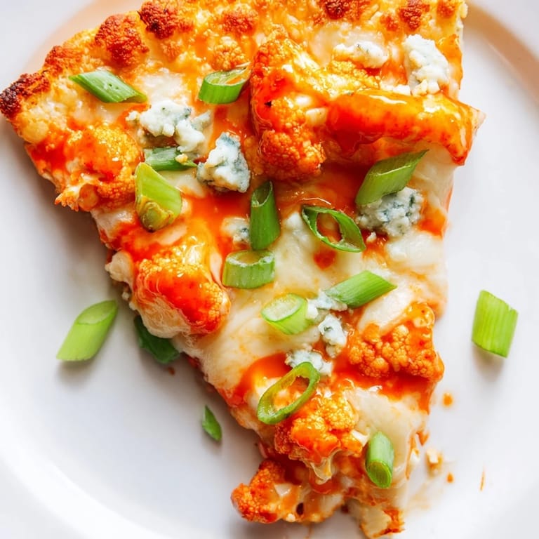 Buffalo Cauliflower Pizza fresh from the oven, featuring a colorful slice with spicy sauce, melted cheese, and a fresh garnish.